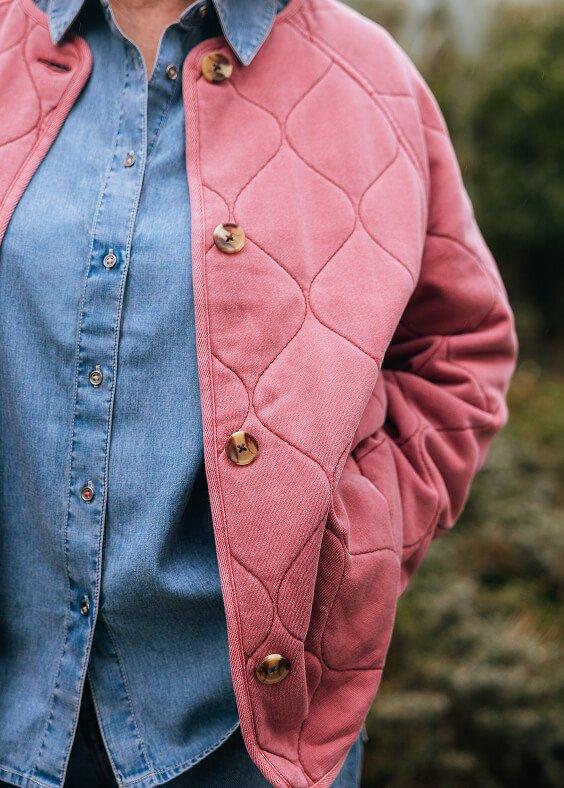 a woman in a pink jacket and blue jeans standing outside